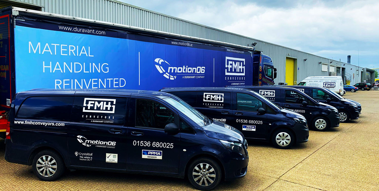 Duravant Lifecycle Services Vehicles parked in front of an FMH Conveyors and Motion06 branded trailer with the phrase 'Material Handling Reinvented' written on it.