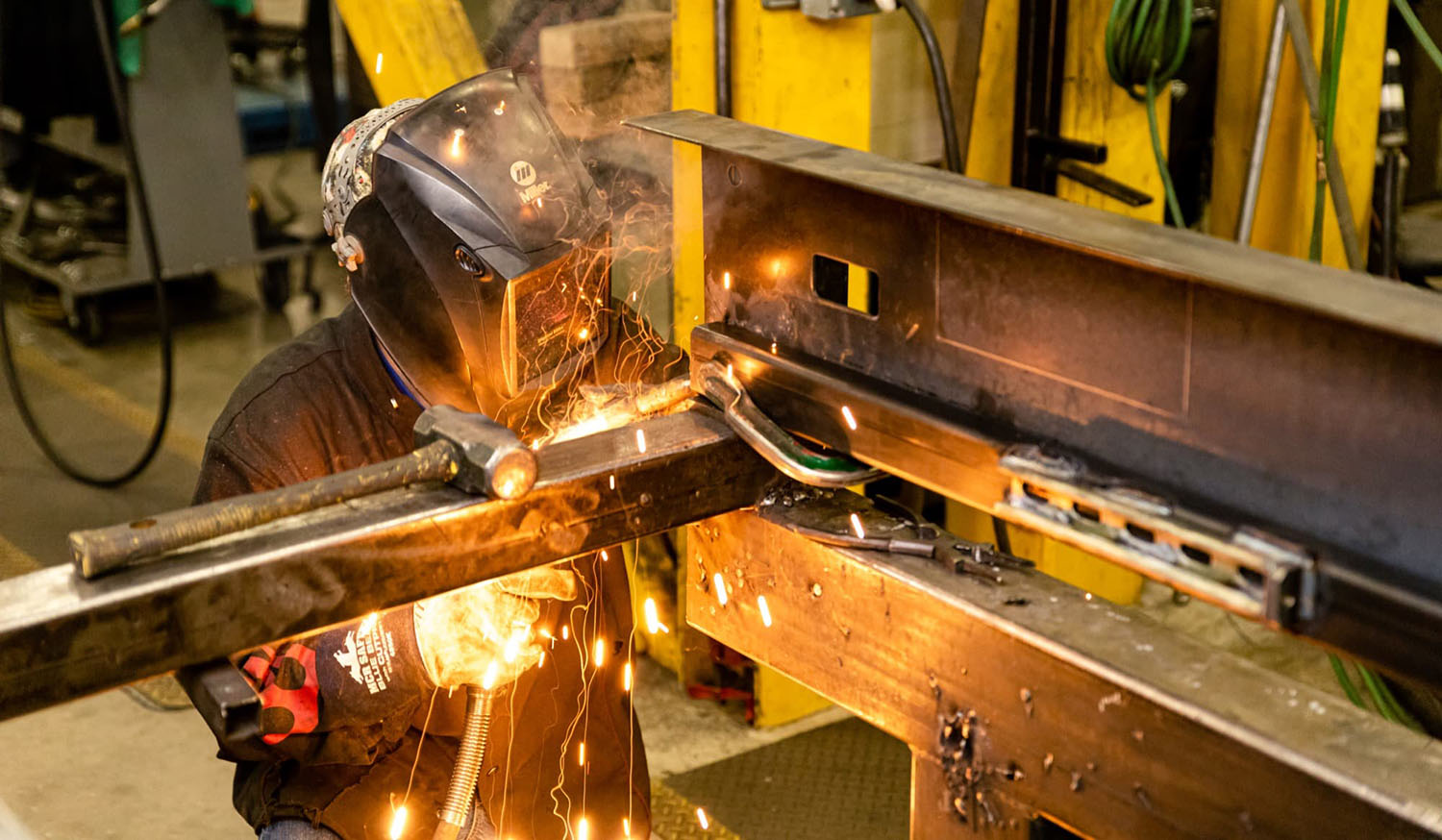 Welder wearing a protective helmet working with sparks in a manufacturing facility, showcasing industrial precision and craftsmanship for the manufacturing and packaging industry.